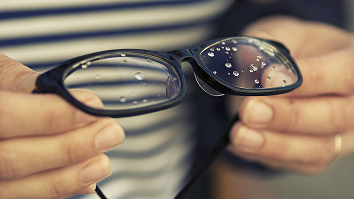 Женщина держит очки с каплями воды на линзах
