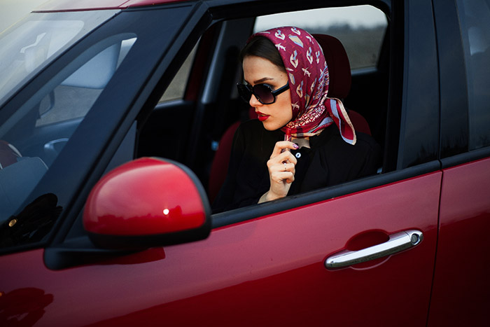 Девушка в слонцезащитных очках и платке сидит в машине