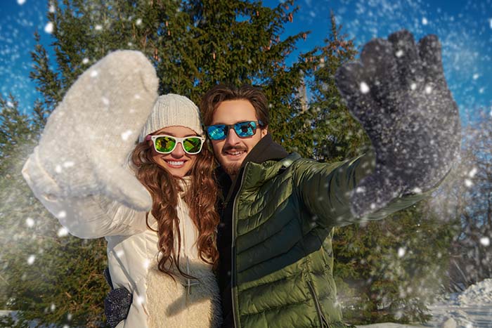 Девушка и парень в солнцезащитных очках, ель и падающий снег на фоне